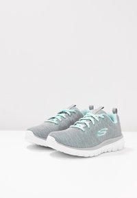 Baskets de sport grises avec une tige en maille respirante, accents bleu clair, bout rond et semelle blanche flexible. Comprend des lacets assortis et une languette au talon.