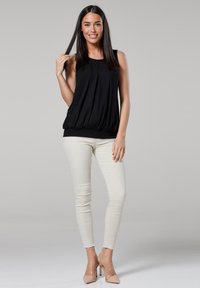Black sleeveless top with gathered front, elastic hem, paired with beige skinny jeans and nude high heels. Smooth fabric, relaxed fit.