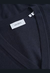 Maglione a V blu marina realizzato in tessuto morbido, caratterizzato da una trama liscia e un'etichetta con "LES DEUX". Cuciture nette lungo i bordi.