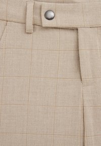 Pantaloni bej în carouri cu un material texturat, având închidere cu un nasture argintiu și pliseuri frontale, evidențiind un model geometric în tonuri subtile.