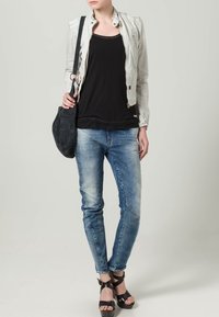 Biała skórzana kurtka motocyklowa, czarny top na ramiączkach, niebieskie obcisłe dżinsy, czarna zamszowa torebka na ramię oraz czarne sandały na paski.