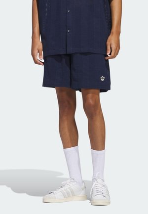 Pantalones cortos de malla azul marino con un patrón texturizado y un pequeño logo bordado, combinados con calcetines blancos de canalé y zapatillas blancas clásicas.