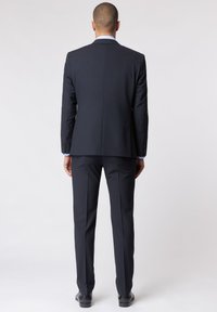 Granatowy garnitur z dopasowaną marynarką o gładkiej fakturze i klapami w kształcie litery notch, w połączeniu z spodniami slim-fit i czarnymi butami wizytowymi.
