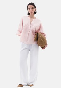 Camicia a righe rosa chiaro con una vestibilità rilassata, abbinata a pantaloni bianchi a gamba larga e una borsa intrecciata marrone. Il look presenta un scollo a V e maniche morbide.