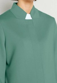 Groen, lichtgewicht kledingstuk met een hoge kraag en een contrasterend wit accent bij de nek. Heeft een eenvoudig, gestroomlijnd ontwerp.