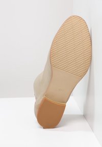 Beiger Knöchelstiefel mit strukturiertem Obermaterial und einer profilierten Gummisohle. Größe 37 ist auf der Sohle eingraviert, mit einer glatten, weichen Oberfläche.