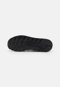 Black rubber shoe sole with textured tread pattern, featuring grooves for grip and a logo imprint, designed for durability and traction.