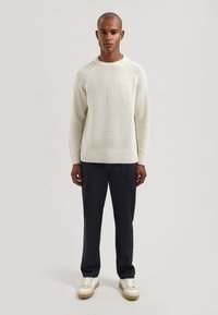 Pull en tricot crème clair avec un motif en relief, manches raglan et poignets côtelés. Assorti à un pantalon foncé et des baskets beiges.