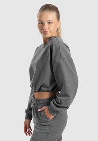 Maglione grigio corto con maniche lunghe, orlo arricciato e logo ricamato; abbinato a pantaloni corti coordinati con vita elasticizzata e tasche.