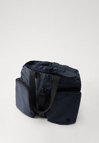 Sac fourre-tout en tissu bleu marine avec des poches zippées de chaque côté et de solides poignées noires. Matériau texturé avec une finition lisse, intérieur spacieux.