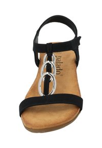 Sandal nera con tre accessori circolari metallici. Presenta una parte superiore simile alla pelle scamosciata, cinturino regolabile e una soletta imbottita di colore beige. Suola piatta.