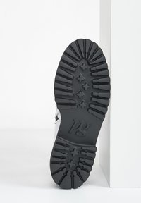 Semelle de chaussure en caoutchouc avec motif texturé présentant des rainures profondes et des formes hexagonales ; marquée du logo "pg" au centre du bas. Principalement noire.