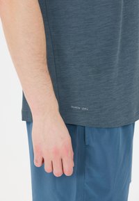 Grå, kortärmad skjorta med ett strukturerat mönster och texten "QUICK DRY" vid fållen, kombinerad med blå shorts.