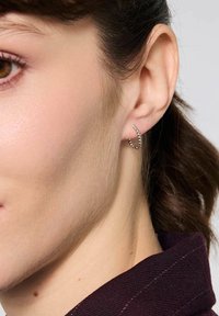 Srebrna kolczyk w kształcie obręczy z teksturowaną powierzchnią, z spiralnym wzorem. Noszony na płatku ucha, z widocznymi naturalnymi włosami i skórą.