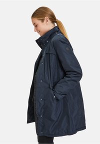 Marineblaue, langärmelige Jacke mit hohem Kragen, Druckknöpfen und seitlichen Taschen. Verfügt über eine strukturierte Oberfläche und einen lässigen Schnitt.