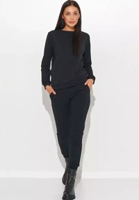 Czarna bawełniana bluza i dopasowane spodnie o luźnym kroju, z bocznymi kieszeniami i prążkowanymi mankietami, zestawione z czarnymi botkami za kostkę.