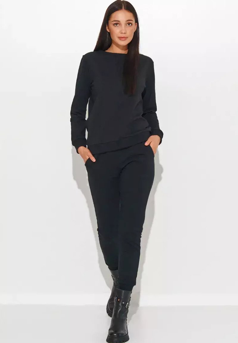 Czarna bawełniana bluza i dopasowane spodnie o luźnym kroju, z bocznymi kieszeniami i prążkowanymi mankietami, zestawione z czarnymi botkami za kostkę.
