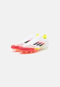 Scarpette da calcio bianche con accenti in gradiente da rosa a giallo, dotate di una tomaia testurizzata, strisce nere e tacchetti multicolori sulla suola.