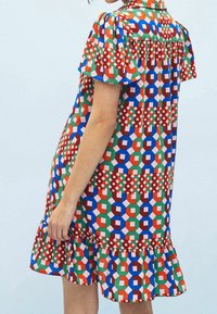 Femme portant une robe à manches courtes, ample, avec un motif géométrique dans des couleurs rouge, vert, bleu et rose sur un fond uni.