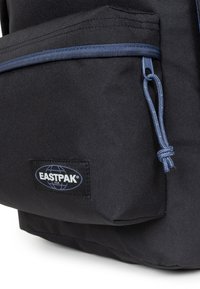 Zaino nero realizzato in nylon testurizzato, con una cerniera accentuata blu e una tasca frontale. Include un'etichetta con il logo Eastpak.