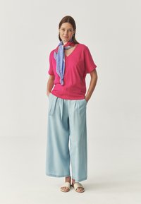 Felroze kortmouw V-hals top, lichtblauwe wijdere broek, en een patroon met een blauwe sjaal. Schoenen zijn crèmewitte slides.