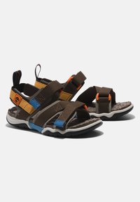 Sandalias marrones con correas ajustables en acentos amarillos, azules y naranjas. Plantilla texturizada, suela de goma y tirador trasero para facilitar su uso.