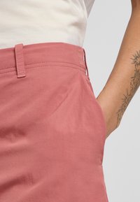 Jupe en tissu rose avec une texture lisse, dotée d'une poche latérale et de détails de couture visibles à la taille.
