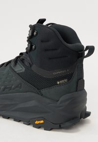 Svart vandringskänga med hög krage, tillverkad av textil och gummi. Har GORE-TEX och Vibram-logotyper, strukturerade mönster och säker snörning.