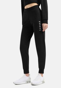 Pantaloni sportivi neri con un design affusolato, realizzati in un materiale morbido e dotati di una comoda vita elastica ampia. Accenti del logo in argento lungo il lato.