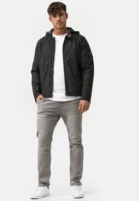 Schwarze Lederjacke mit gerippten Schulterakzenten und einem grauen Hoodie, kombiniert mit hellgrauen Jeans und weißen Sneakern.