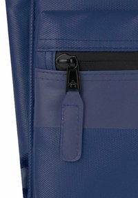 Blå teksturert stoffveske med svart glidelås og matchende dragrem. Designet inkluderer en frontlomme for ekstra lagring.