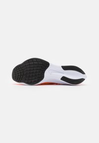 Semelle de chaussure de sport blanche avec une semelle en caoutchouc noir, présentant un motif texturé et un détail de logo visible au centre.