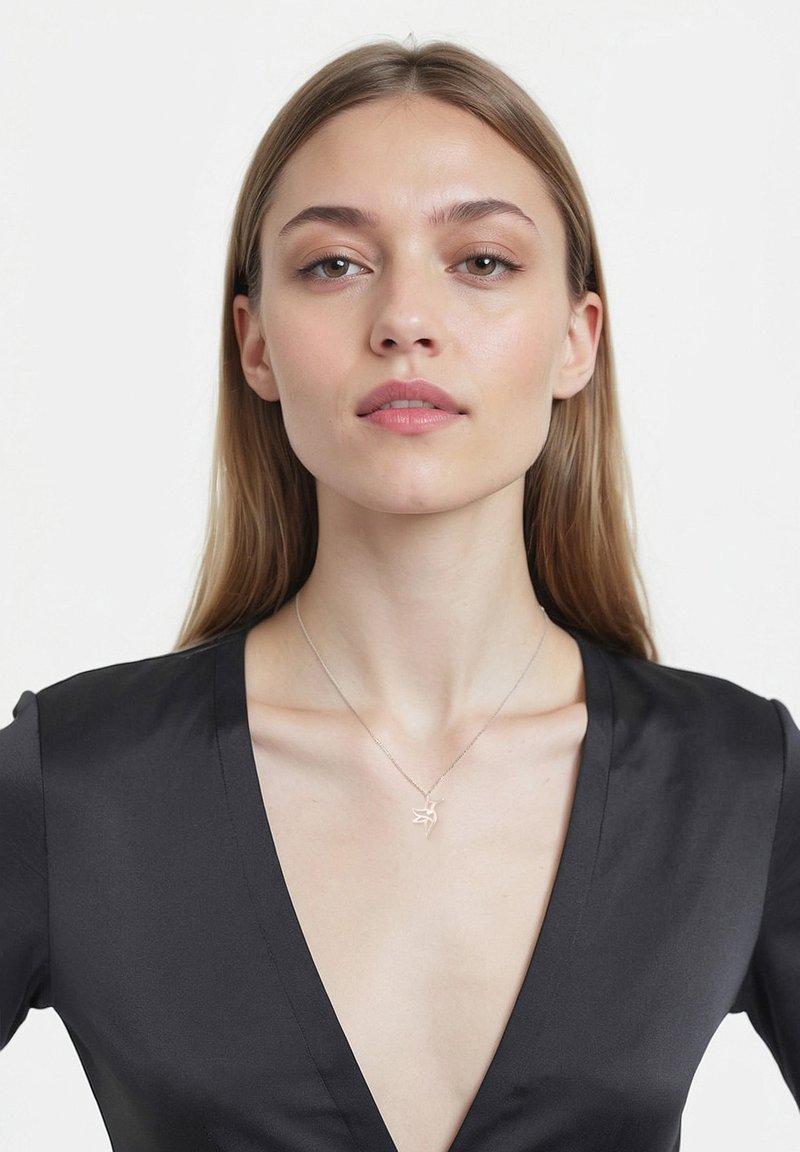 Sølv fuglependant halskæde på en delikat kæde, båret over en dyb v-hals sort satin-top, der har en glat tekstur og et minimalistisk design.