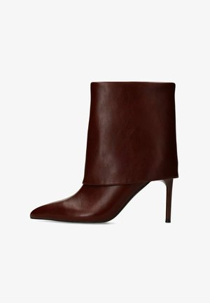 Donkerbruine leren laars tot halverwege de kuit met hoge hak, spits toelopende neus en smalle stilettohak, getoond op een witte achtergrond.