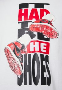 Bílý tričko s červeným a černým grafickým potiskem tenisek a tučným textem "TO MUSELY BÝT TY BOTY." Tenisky mají výjimečné detaily.