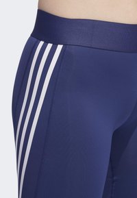 Námořnické legíny se širokým elastickým pasem mají tři bílé pruhy po vnější straně a jsou vyrobeny z hladkého, elastického materiálu.