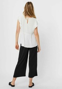 Top peplum bianco leggero con maniche a volant e schiena a forma di chiave, abbinato a pantaloni neri larghi e sandali neri flat.