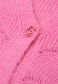 Roze gebreide cardigan met ribbeltextuur, voorzien van een ronde, glanzende knop met een roze centrum en een zachte, pluizige afwerking.