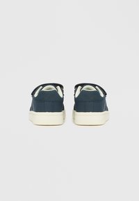 Tmavě modré tenisky s hladkým koženým svrškem, texturovanými bočními panely a bílou gumovou podrážkou; mají dvě pásky na suchý zip pro zavírání.