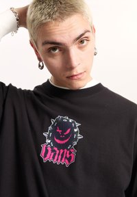 Camiseta de algodón negra con un gráfico colorido de una bola espinosa con una cara sonriente y la palabra "Vans" en letras estilizadas y en negrita.