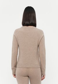 Beige strikket genser med rund hals og ribbestrikkede mansjetter, vist fra baksiden. Myk tekstur, tettsittende design og sømløs konstruksjon.
