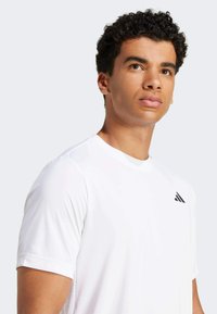 White athletic t-shirt with short sleeves, featuring a black logo on the chest. The fabric appears smooth and lightweight.