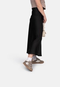 Leopard print shoes with white accents, paired with black flowing skirt and white ankle socks. Compact beige bag held in hand.