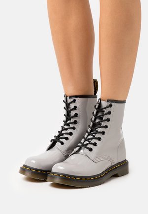 Bottes cheville en cuir verni gris avec lacets noirs, bout rond, couture jaune le long de la semelle et accents texturés noirs en haut.