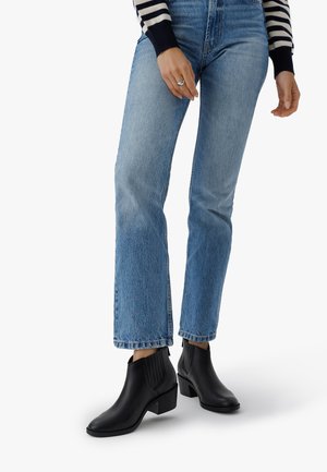 Person, die hellblaue gerade Jeans, schwarze Leder-Ankle-Boots mit Blockabsatz und ein navy-weiß gestreiftes Langarmoberteil trägt.