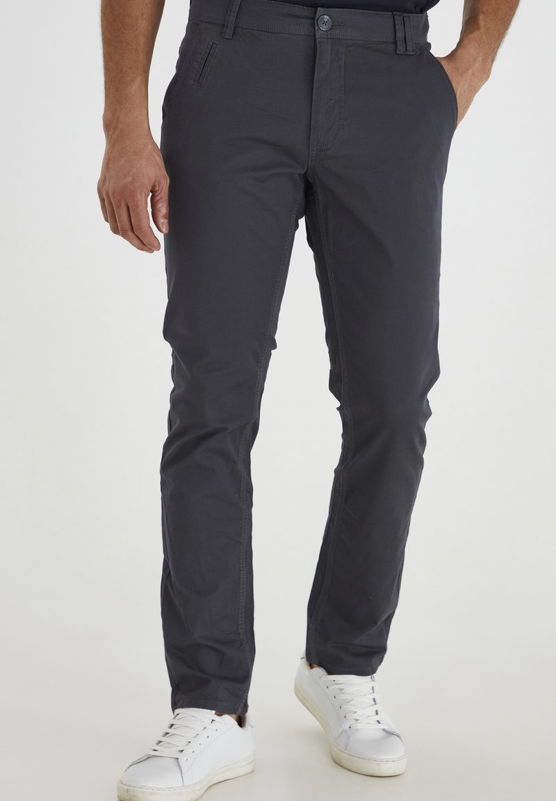 Dark gray chino pants, slim fit, made of cotton blend, with a button closure and side pockets. Paired with white sneakers.