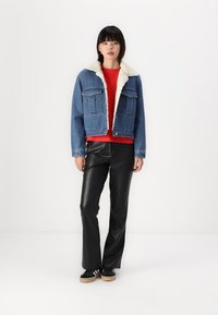 Veste en denim avec col en fausse fourrure crème, deux poches poitrine et fermeture à boutons sur le devant. Haut rouge, pantalon en faux cuir noir et baskets noires.