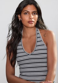 Sort-hvidstribet haltertop med dyb V-udskæring, ribbet tekstur og kontrastfarvet kant. Modellen har langt mørkt hår og en skuldertatovering.