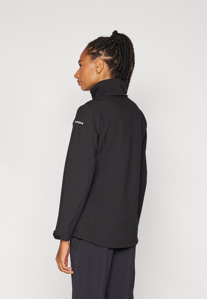 Schwarze Jacke mit hohem Kragen, weichem Material und langen Ärmeln. Besitzt ein Logo am linken Arm und eine lockere Passform.