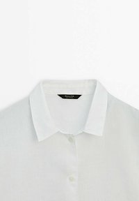Jasny lniany shirt z klasycznym kołnierzykiem, zapinany na guziki z przodu oraz delikatną teksturą. Etykieta z nazwą marki.
